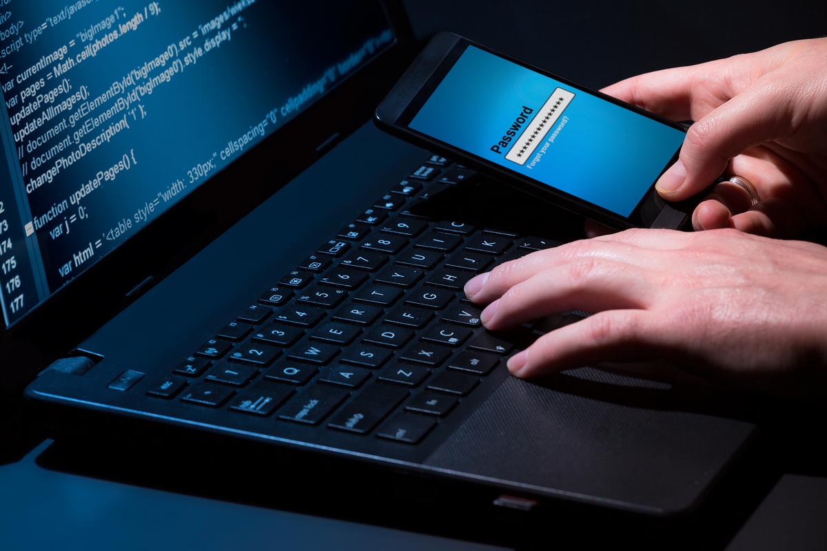 Man working on laptop while entering password to mobile phone