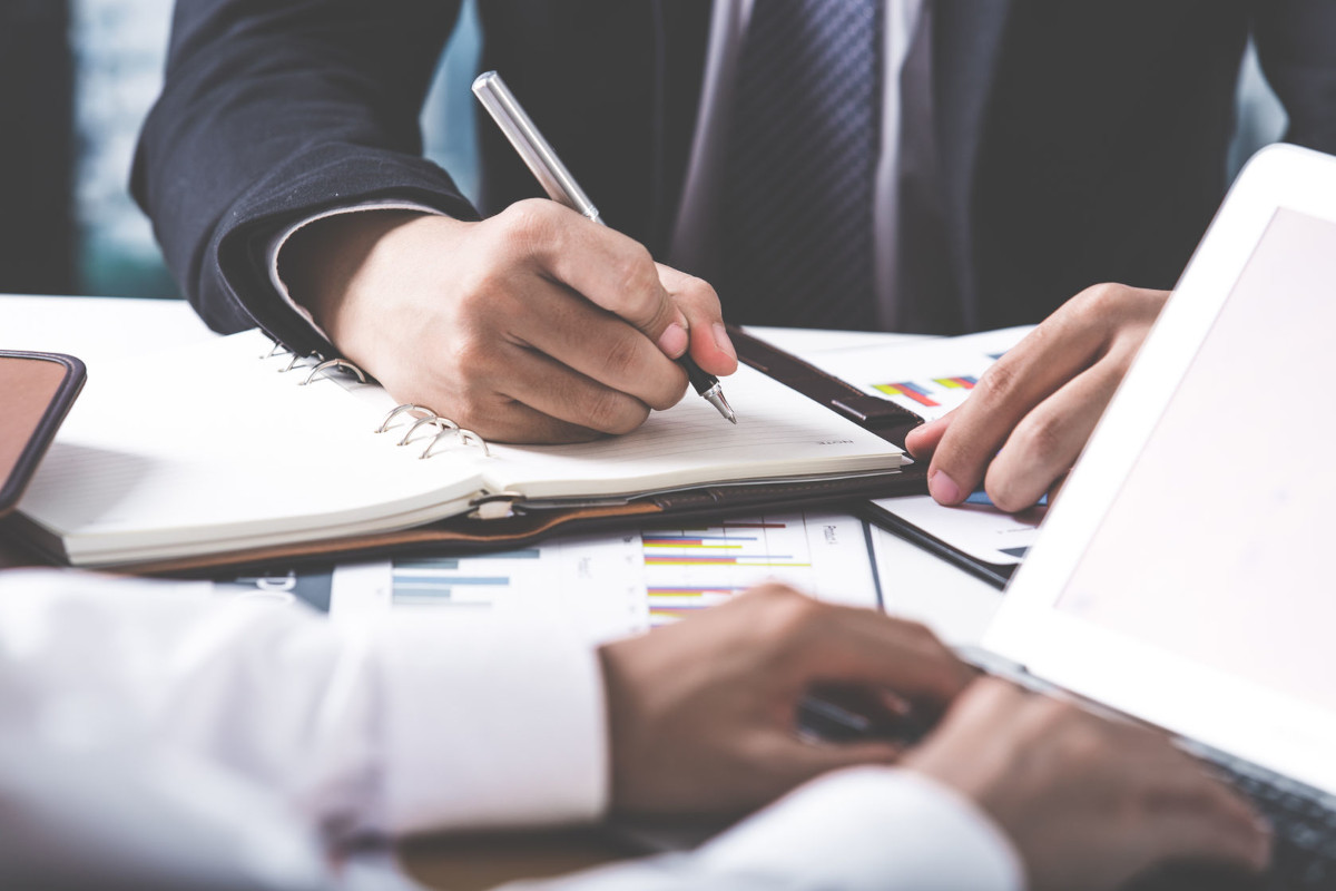 A businessman writing on a notepad with charts on the table