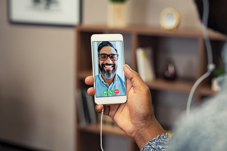 Closeup hands of african man holding smartphone doing video calling with friend. Portrait of latin man with beard on conversation with businessman on smartphone. Man video conferencing with mature casual man.