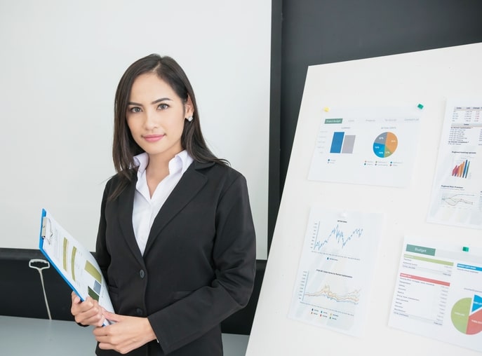 Smiling businesswoman crossed arm with chart background in office. Young Asian woman successful in small business