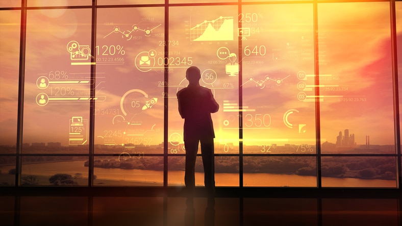 Silhouette of a man in a huge office in front of large windows viewing corporate infographics.